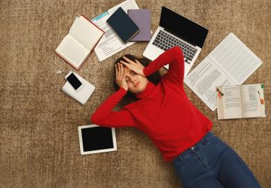 Student surrounded by study material, looking stressed